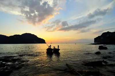 two boats sitting in the water at sunset at Twin Palms Hostel Phi Phi in Phi Phi Don