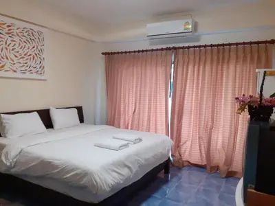 a bedroom with a bed with white sheets and a television at NB House in Karon Beach
