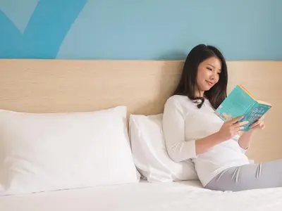 a woman sitting on a bed reading a book at HOP INN Phuket in Phuket Town