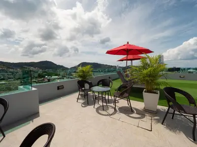 a patio with chairs and a table and a red umbrella at Neon Patong in Patong Beach
