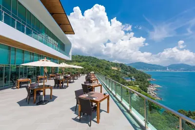 a balcony with tables and chairs and the ocean at Wyndham Grand Phuket Kalim Bay in Patong Beach