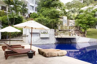 a pool with two chairs and an umbrella and a table and benches at Kamala Hills Serviced Apartments in Kamala Beach
