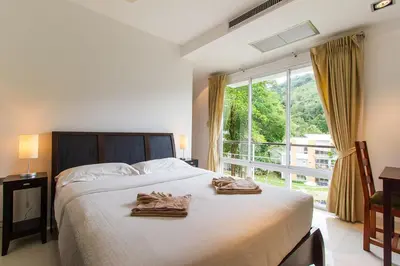 a bedroom with a bed and a large window at Kamala Hills Serviced Apartments in Kamala Beach