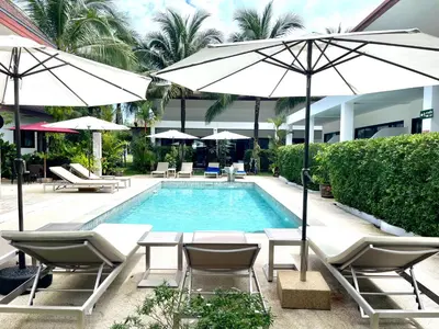 a pool with chairs and umbrellas next to a building at Lotus Bleu Resort & Restaurant in Rawai Beach