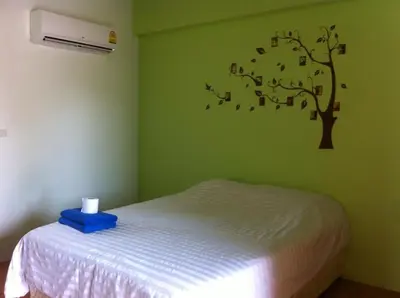 a bedroom with a bed with a tree on the wall at Six Pack Cottage in Chalong