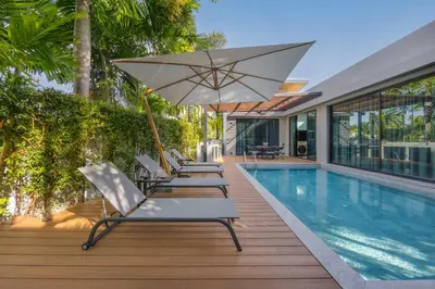 a row of lounge chairs and an umbrella next to a swimming pool at VILLA PULAU 3 bedroom Baan Bua Estate in Nai Harn Beach