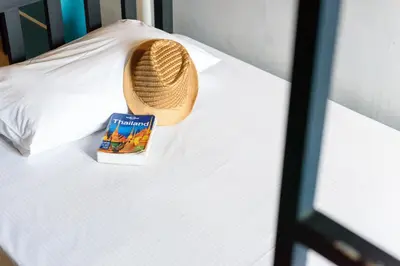 a book and a straw hat sitting on a bed at Hip Hostel - SHA Plus in Patong Beach