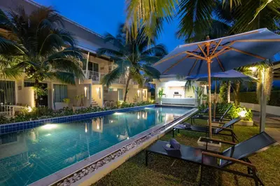 a swimming pool with an umbrella and chairs next to a house at Impress Resort in Thalang