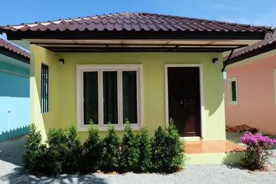 a small yellow and pink house with a door at Maikhao Beach Guest House in Mai Khao Beach