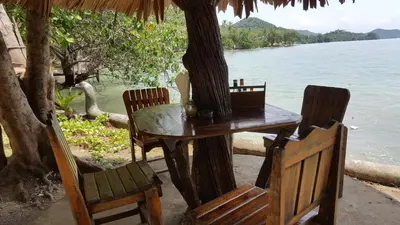 a table and chairs under a tree next to the water at Sabai Corner Bungalows - SHA Extra Plus in Ko Yao Noi
