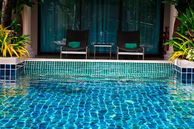 a blue swimming pool with two chairs and a table at Phuket Graceland Resort and Spa in Patong Beach