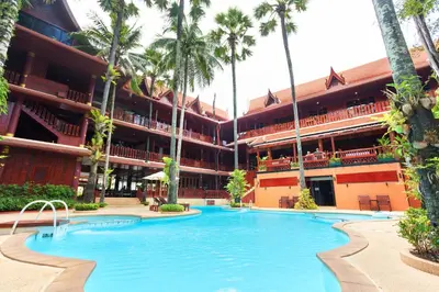 a swimming pool in front of a building with palm trees at Royal Phawadee Village Patong - 2 Minutes walk to the beach in Patong Beach