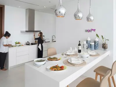 a woman standing in a kitchen with a table with food at Malaiwana Residences in Nai Thon Beach