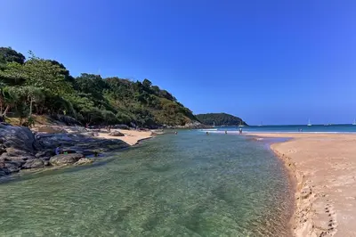 a beach with a sandy shore with people in the water at Mangosteen Ayurveda & Wellness Resort - SHA Plus in Rawai Beach