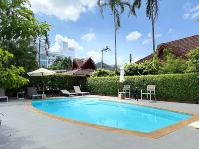 a swimming pool with chairs and a table and trees at Family Bungalow Kamala in Kamala Beach