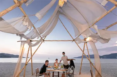 a group of people sitting at a table under a tent on the beach at Baan Laimai Beach Resort & Spa - SHA Extra Plus in Patong Beach