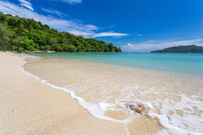 a sandy beach with water and trees in the background at Rosewood Phuket in Patong Beach