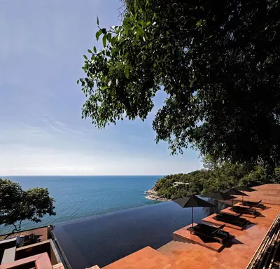 a pool with chairs and umbrellas next to the ocean at Paresa Resort Phuket in Kamala Beach