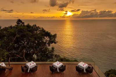 a sunset over the water with umbrellas on a deck at Paresa Resort Phuket in Kamala Beach
