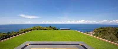 a large grassy field with a view of the ocean at Paresa Resort Phuket in Kamala Beach