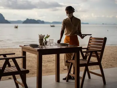 a woman standing next to a table on the beach at Tup Kaek Sunset Beach Resort-SHA Plus in Tab Kaek Beach