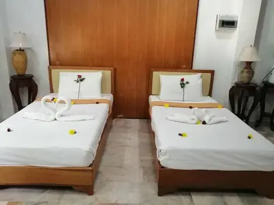 two beds in a room with white sheets and flowers at Tony Home and Restaurant in Karon Beach