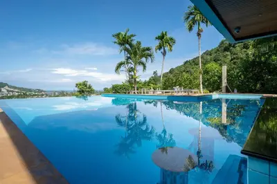 a pool with palm trees and a mountain in the background at Baan Chom View Kamala - SHA Plus in Kamala Beach