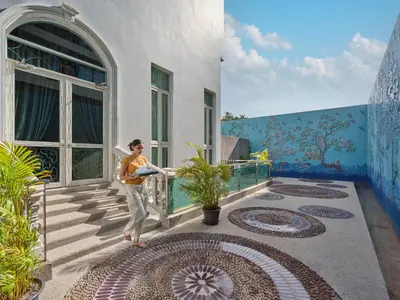 a woman standing on the porch of a house with blue walls at The Kee Resort & Spa in Patong Beach