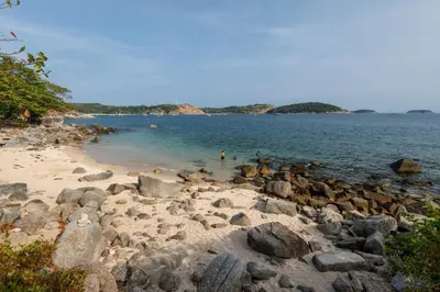 a rocky beach with people swimming in the water at Baan Krating Phuket Resort Naiharn-SHA Plus in Nai Harn Beach