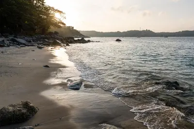 a beach with the sun shining on the water at Baan Krating Phuket Resort Naiharn-SHA Plus in Nai Harn Beach