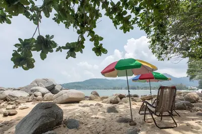 two chairs and an umbrella on a beach at Kamala Beach Estate Resort - SHA Extra Plus in Kamala Beach