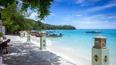 a man sitting on a beach with boats in the water at Phi Phi Andaman Beach Resort in Phi Phi Don