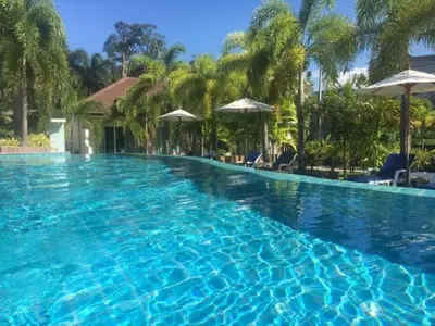 a large blue swimming pool with trees and umbrellas at PS Hill Resort Phuket Patong - SHA Plus in Patong Beach