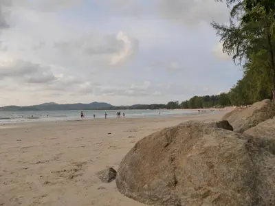 a beach with people in the water and a large rock at Marisa Garden Bungalow in Bang Tao Beach