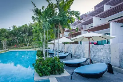 a swimming pool with chairs and umbrellas next to a building at Chalong Chalet Resort in Chalong