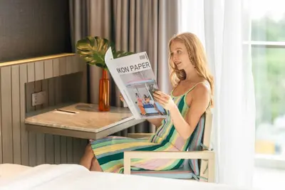 a woman sitting in a chair reading a magazine at Hotel IKON Phuket - SHA Extra Plus in Karon Beach