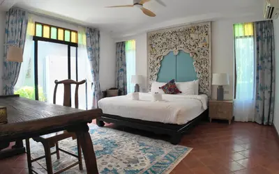 a bedroom with a bed and a table and windows at Baleeyan in Thalang