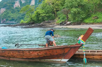 a man standing in a wooden boat in the water at Phi Phi Sunset Bay Resort in Phi Phi Don