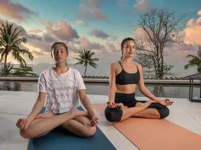 two women sitting in a yoga pose next to a pool at Naam Sawan in Ban Pa Khlok