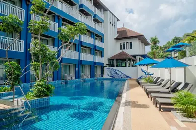a swimming pool in front of a building with chairs and umbrellas at Blue Tara Hotel Krabi Ao Nang in Ao Nang Beach