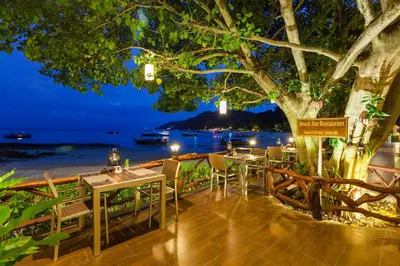 a restaurant with tables and chairs under a tree at night at Phi Phi Natural Resort in Phi Phi Don