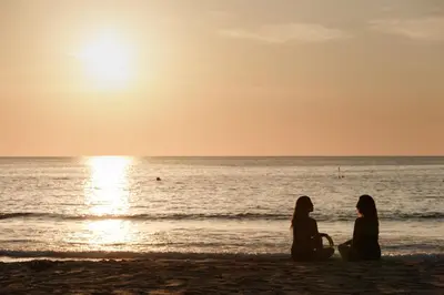 two women sitting on the beach watching the sunset at The Surin Phuket in Surin Beach