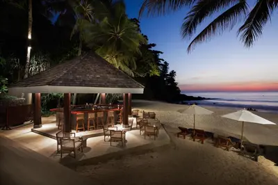 a restaurant on the beach with chairs and tables and umbrellas at The Surin Phuket in Surin Beach