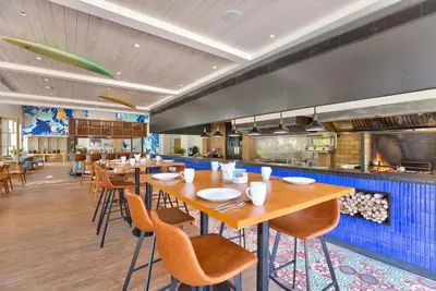 a restaurant with wooden tables and chairs and a kitchen at OUTRIGGER Surin Beach Resort in Surin Beach