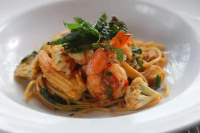 a white plate of pasta with shrimp and vegetables at Woraburi Phuket Resort & Spa - SHA Plus in Karon Beach