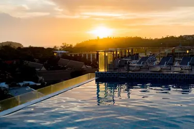 a pool with chairs and the sunset in the background at Ozone Condotel by RESAVA in Kata Beach
