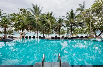 a large swimming pool with palm trees and chairs at Impiana Beachfront Resort Patong, Phuket in Patong Beach