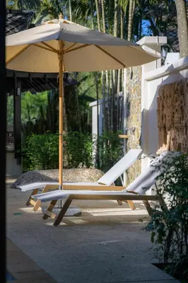 two lounge chairs and an umbrella on a sidewalk at The Hotspring Beach Resort & Spa - SHA Extra Plus in Natai Beach
