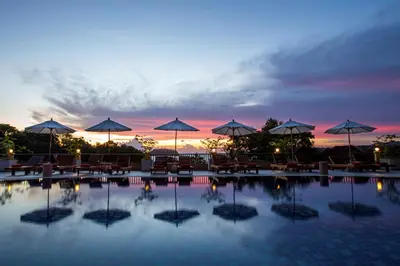 a swimming pool with tables and umbrellas at sunset at Chanalai Garden Resort, Kata Beach in Kata Beach