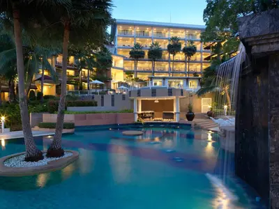 a pool with palm trees in front of a building at Chanalai Flora Resort, Kata Beach in Kata Beach